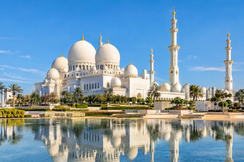 A white marble mosque with domes and minarets reflected in a pool in Abu Dhabi