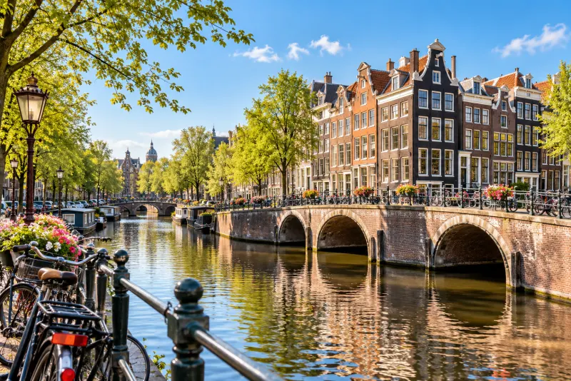 Brick canal houses, an arched stone bridge and bicycles under spring trees in Amsterdam