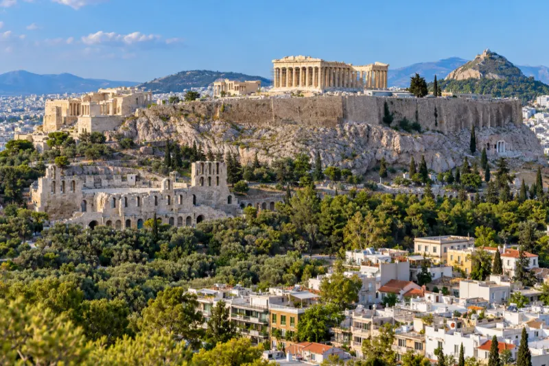 The Parthenon on its rocky hill above pine trees and white rooftops in Athens