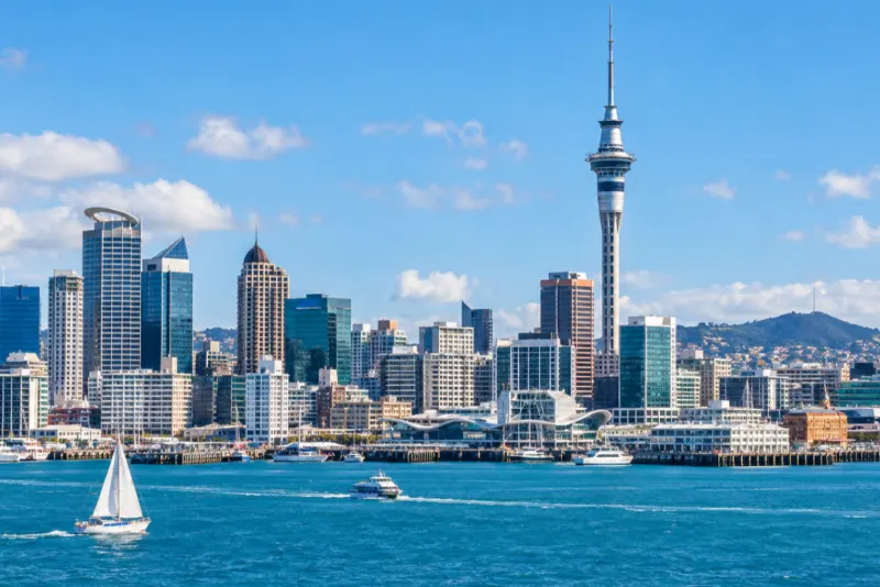 A tall observation tower and glass skyscrapers above a harbour with a sailboat in Auckland
