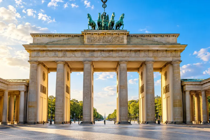 A neoclassical gate with tall columns and a bronze horse-drawn chariot in warm light in Berlin