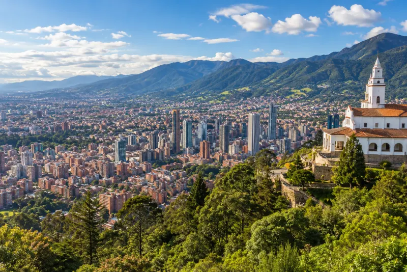 A hillside white church above a city of brick towers with green mountains behind in Bogota