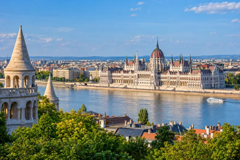 A riverside parliament with a red dome seen past white stone turrets in Budapest