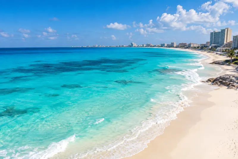 A white sand beach and bright turquoise sea with a hotel strip beyond in Cancun