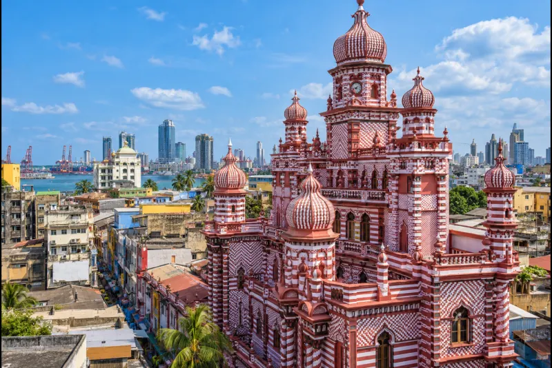 A red and white striped mosque with onion domes above the rooftops and harbour of Colombo