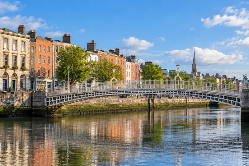 A white pedestrian bridge over a calm river beside red-brick Georgian houses in Dublin