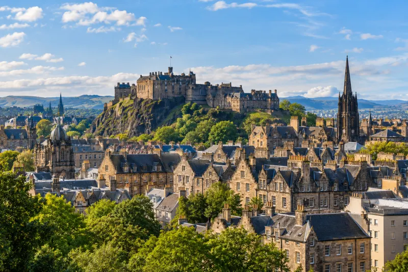 A hilltop castle above stone tenements and a dark church spire in Edinburgh