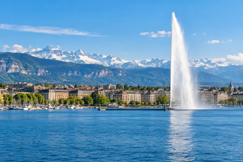 A tall water jet on the lake with snowy mountains rising behind the city in Geneva