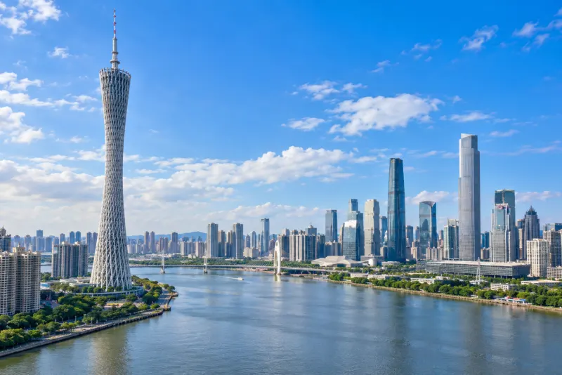A lattice-patterned tall tower and glass skyscrapers along a wide river in Guangzhou