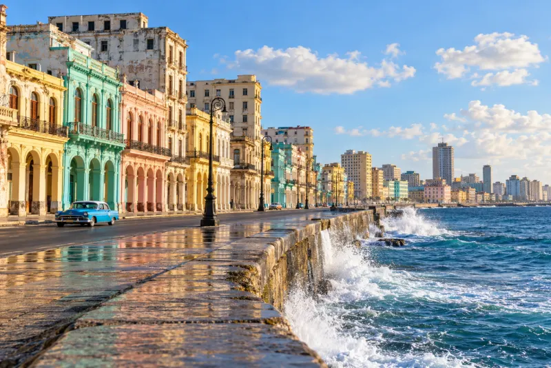 Pastel colonnaded buildings, a vintage car and waves crashing on the seawall in Havana