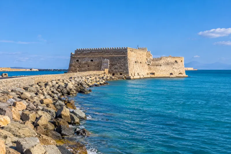 A stone sea fortress with battlements on a breakwater above blue water in Heraklion
