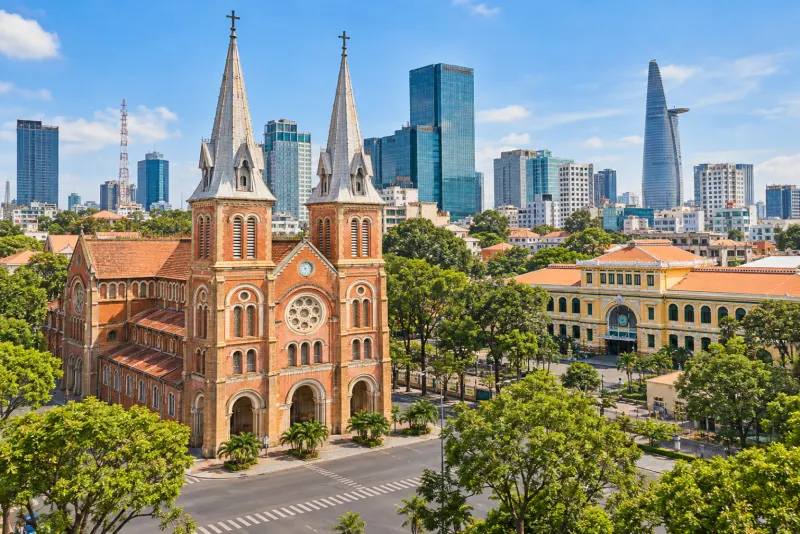 A red-brick twin-spired cathedral and a yellow post office beside towers in Ho Chi Minh City