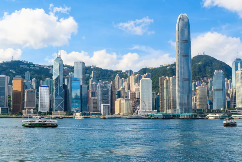 Harbour ferries below a crowd of skyscrapers and a green hill in Hong Kong