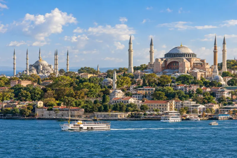 A great domed mosque and tall minarets above the Bosphorus with a passenger ferry in Istanbul