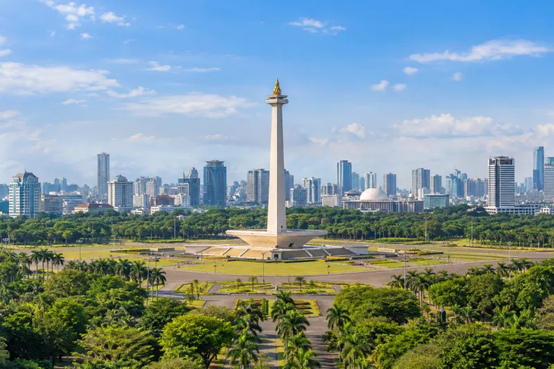A tall golden-topped monument on a green plaza with a city skyline behind in Jakarta
