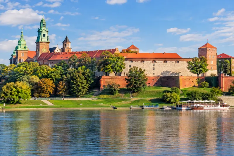 A hilltop castle with copper roofs and green spires above a river in Krakow