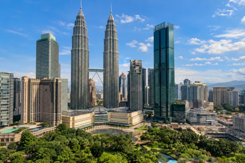 Two tall silver skyscrapers joined by a bridge above a park in Kuala Lumpur