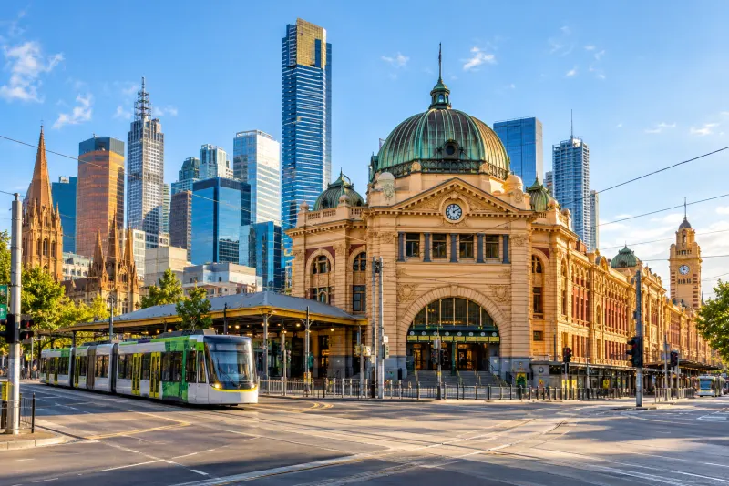 A grand domed railway station with a green tram and glass towers in Melbourne