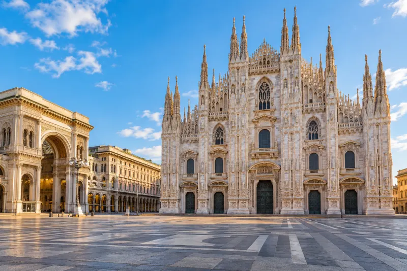 The ornate white marble cathedral and a glass-roofed arcade on an empty square in Milan