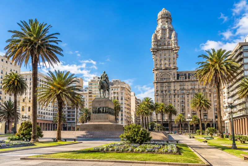 A tall ornate tower and an equestrian statue among palms in Montevideo