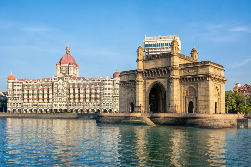 The Gateway of India arch beside a grand domed hotel on calm water in Mumbai