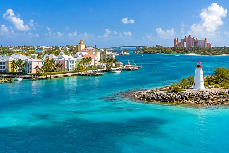 Pastel waterfront houses, a small white lighthouse and a pink resort across turquoise water in Nassau