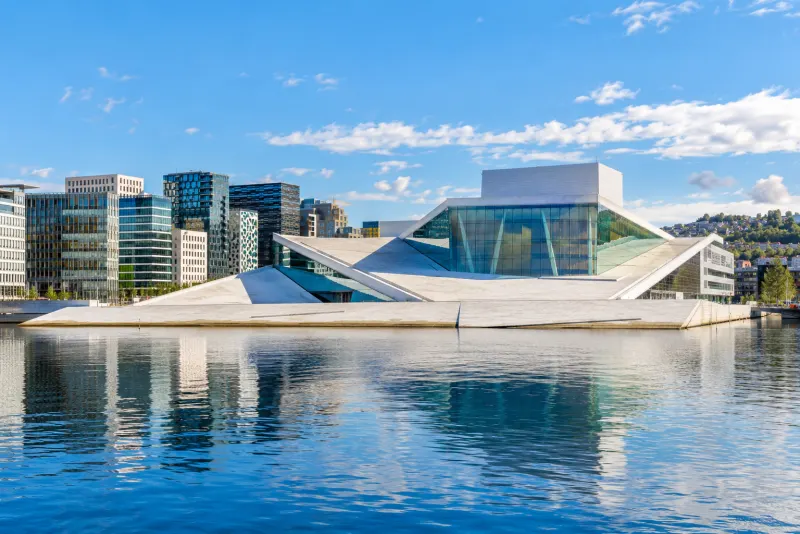 A white angular opera house with a glass front beside calm harbour water in Oslo