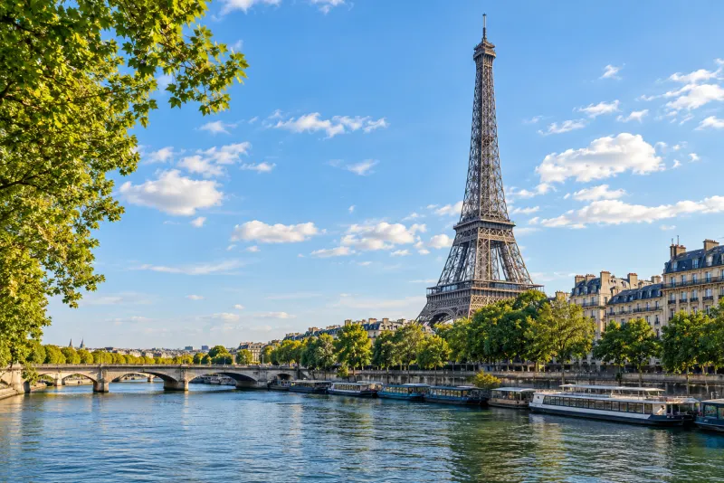 The Eiffel Tower above the Seine and a stone bridge on a sunny day in Paris
