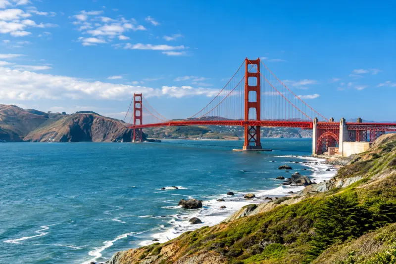 The red Golden Gate Bridge spanning blue water beyond a rocky shore in San Francisco
