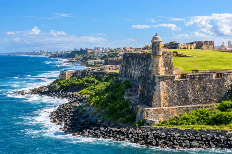 A weathered stone fortress with a lookout turret above rocky shore and surf in San Juan