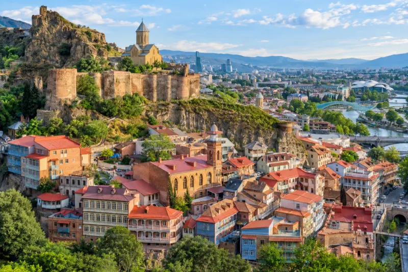 Old houses with wooden balconies and a hilltop fortress and church above a river in Tbilisi